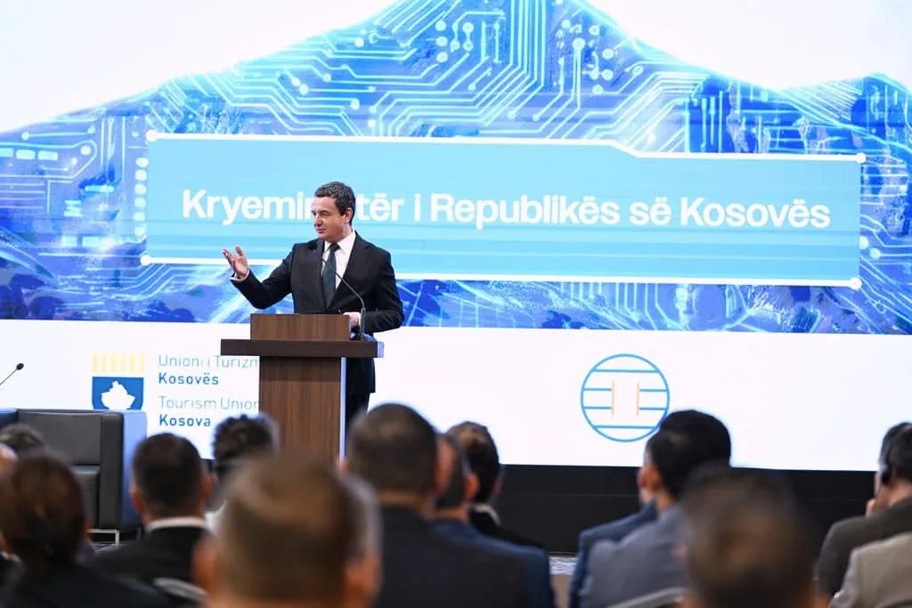 Kosovo's prime minister addresses an audience before an AI-themed backdrop and the Union i Turizmit Kosovës logo.